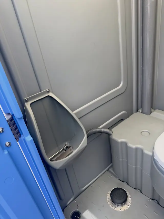 Inside a portable toilet showing a wall-mounted urinal