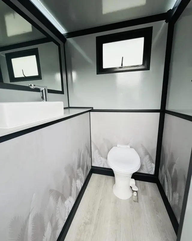 Inside a restroom trailer stall showing a flushing toilet and wall finish
