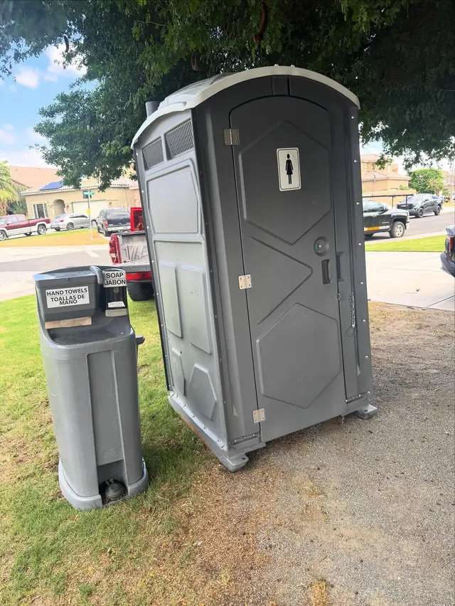 Gray portable toilet next to a hand wash station on a level lawn